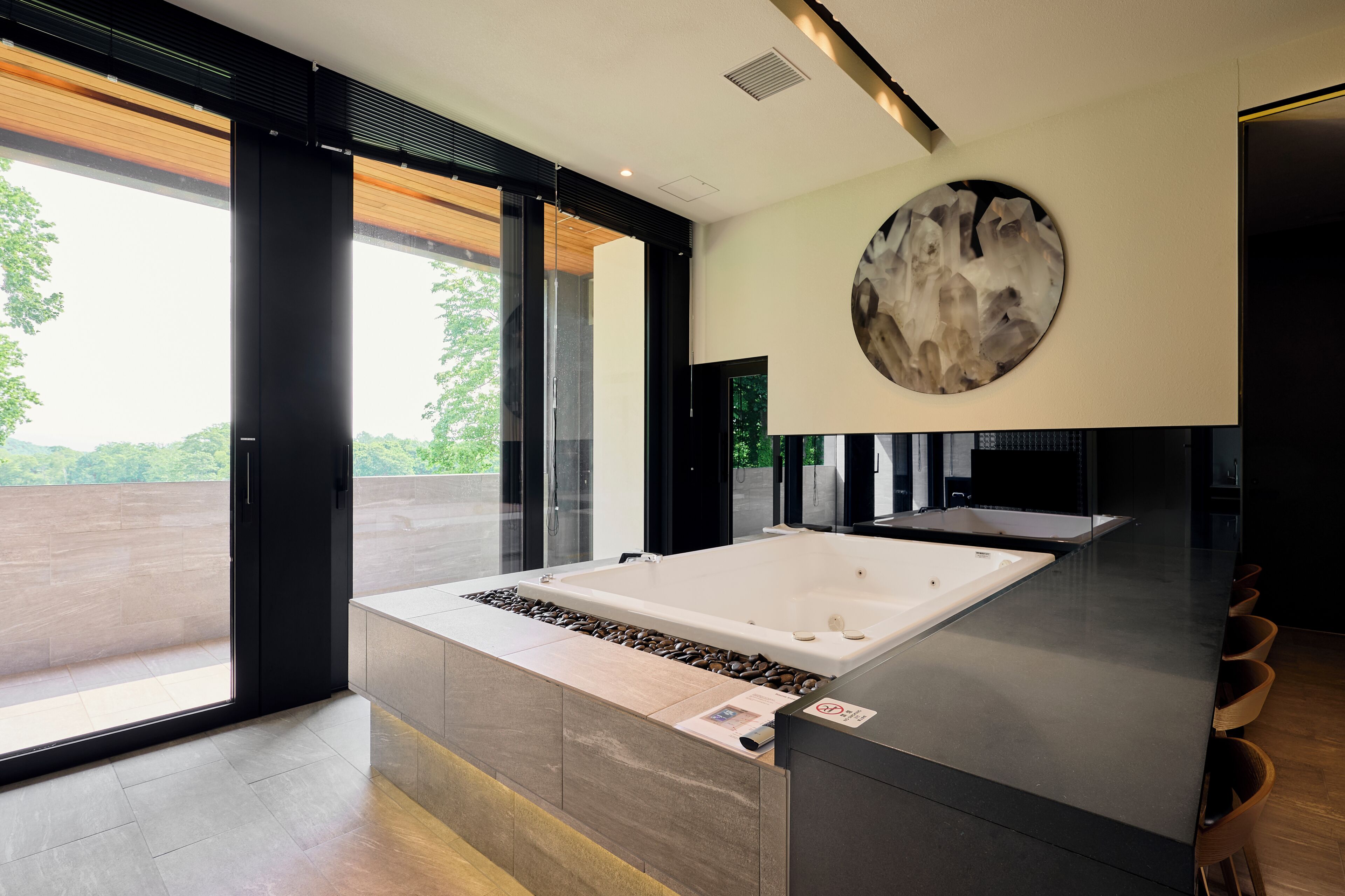Un baño moderno con una bañera grande, una pieza de arte circular en la pared y vistas a zonas verdes al exterior.
