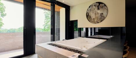 Un baño moderno con una bañera grande, una pieza de arte circular en la pared y vistas a zonas verdes al exterior.
