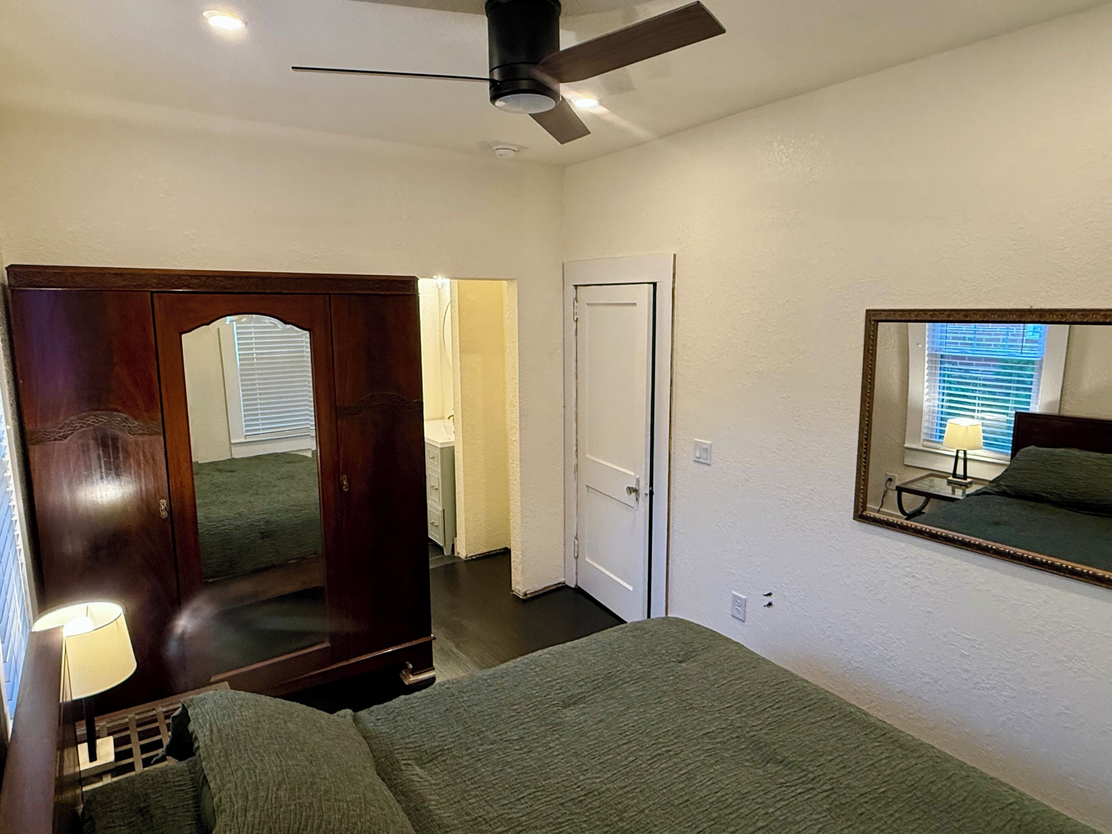 A bedroom with a bed, a dresser, a mirror, and a ceiling fan.