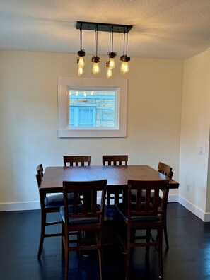 A dining area with a table and chairs, a ceiling light fixture, and a framed picture on the wall.