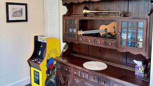 Une pièce avec un meuble en bois contenant des instruments de musique, un tableau encadr é au mur et une borne d’arcade jaune.