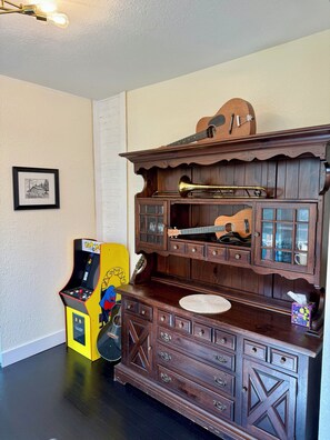 A room with a wooden cabinet containing musical instruments, a framed picture on the wall, and a yellow arcade machine.