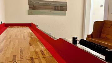 Une table de jeu de palet, avec un jeu de fléchettes fixé au-dessus, un plancher en bois et une zone recouverte d’une moquette rouge.
