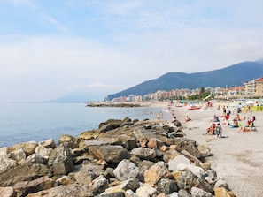 Ein felsiger Strand mit Blick auf das Meer und Gebäude im Hintergrund.