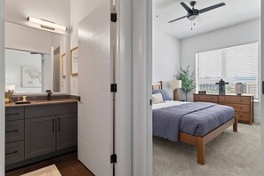 Ein Schlafzimmer mit einem Bett, einem Nachttisch, einer Kommode, einem Fenster mit Jalousien und einem Deckenventilator.