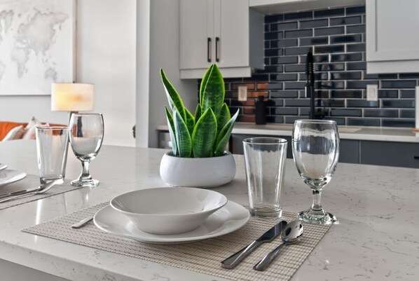A modern kitchen with a marble countertop, a potted plant, and a dining setup with a bowl, glasses, and cutlery. - Modern 1BR Apt. Long Term. Downtown. Pool. Parking (Birmingham)