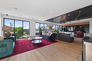 A spacious living room with a large window, a red carpet, and a modern kitchen area. - Modern 1BR Apt. Long Term. Downtown. Pool. Parking (Birmingham)