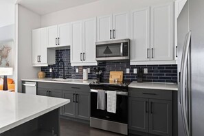 A modern kitchen with white cabinets, a stainless steel refrigerator, and a microwave. - Modern 1BR Apt. Long Term. Downtown. Pool. Parking (Birmingham)