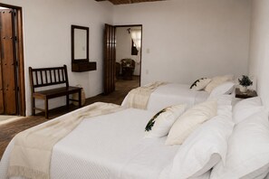 A bedroom with two beds, a bench, a mirror, and a door.
