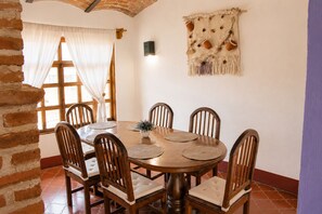 Uma sala de jantar com uma mesa redonda de madeira, seis cadeiras e um adorno pendurado na parede.