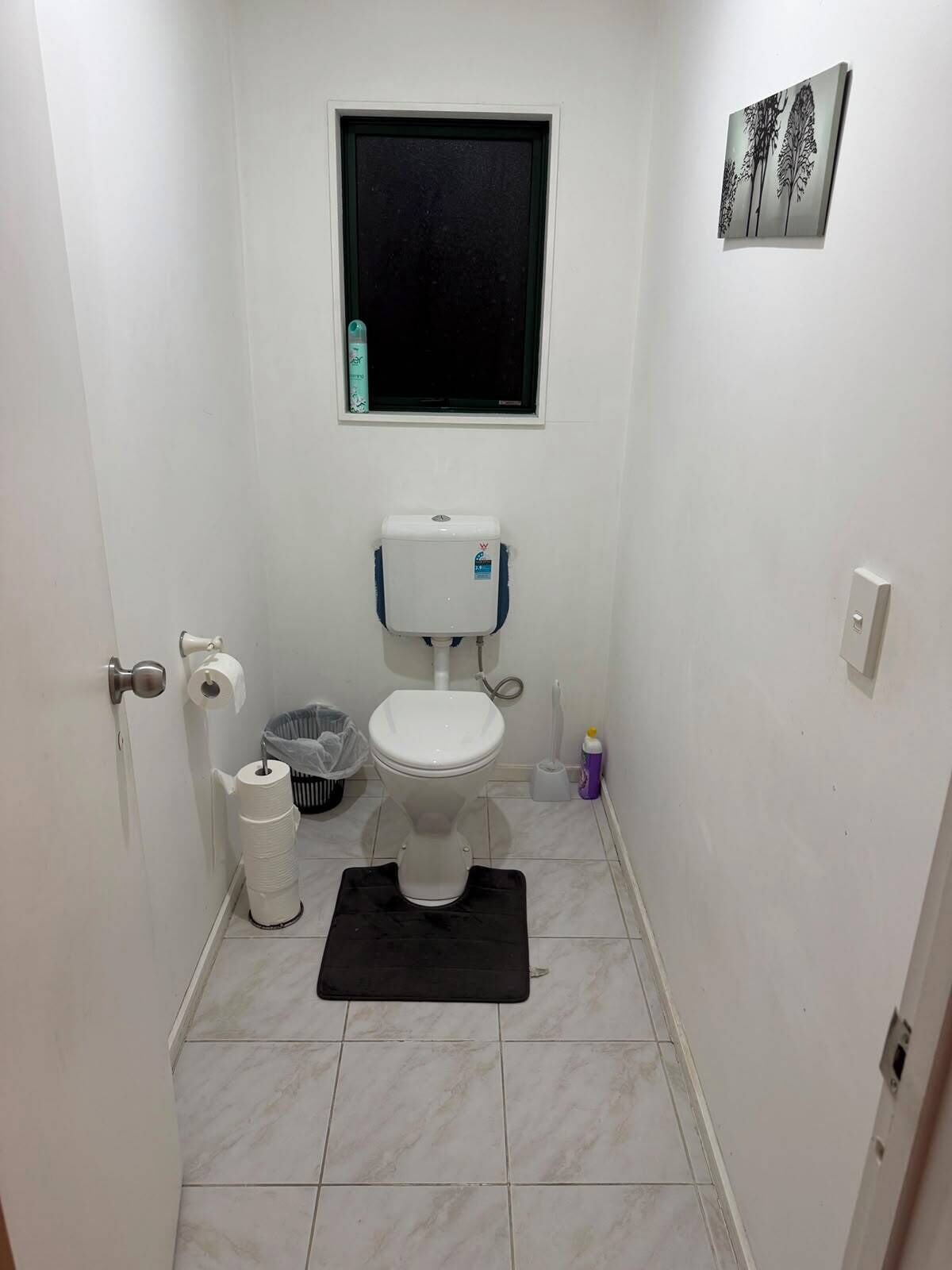 Ein kleines, sauberes Badezimmer mit Toilette, einem Fenster und einer schwarzen Matte auf dem Boden.