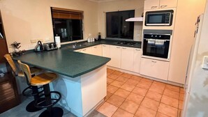A compact kitchen with a central island, a microwave, an oven, and a sink. - Stay Local, Live Like a Kiwi: Bright & Spacious 3BR Green Home (New Lynn)