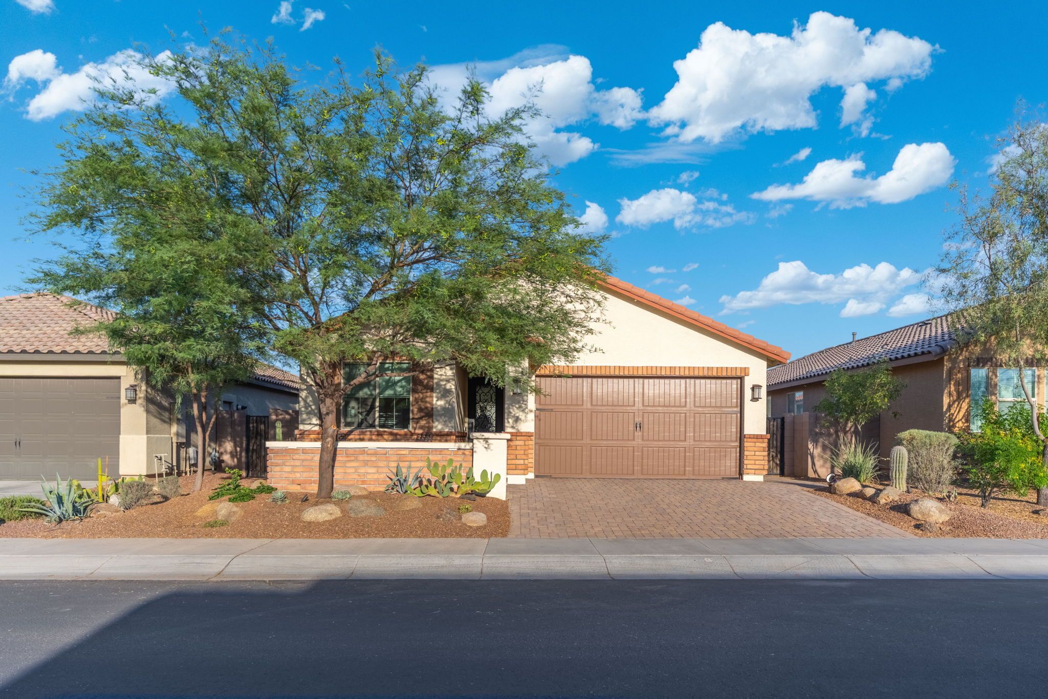 A residential house with a garage, a covered driveway, and a landscaped front yard with various plants and a tree.