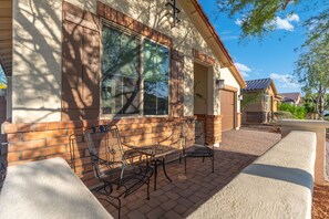Une maison avec une façade en briques, un patio couvert avec des chaises et une table en métal, et une porte de garage.