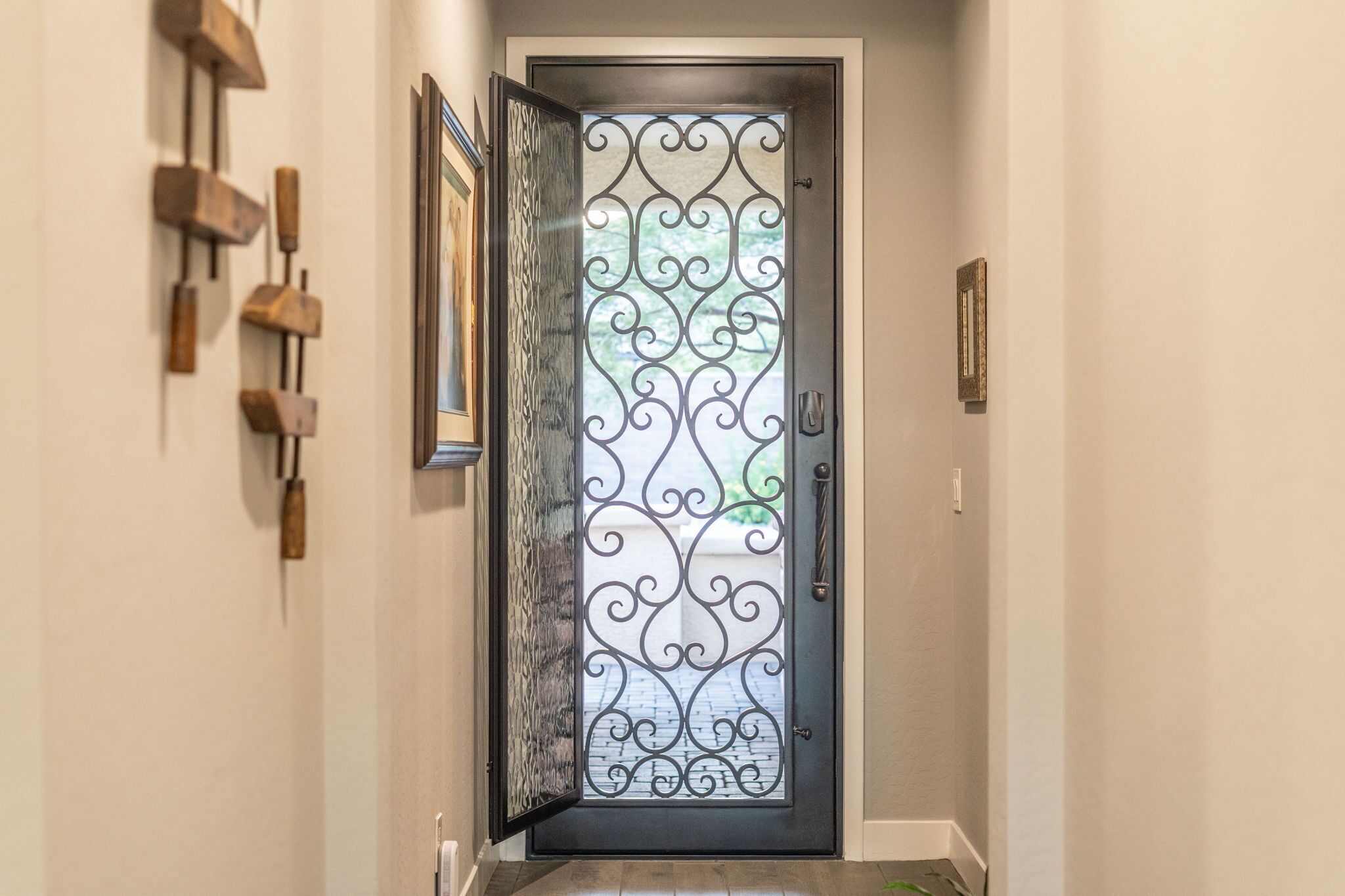 Un pasillo con una puerta metálica decorativa, una lámpara de pared y un cuadro enmarcado.