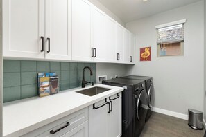 A modern kitchen with white cabinets, a stainless steel sink, and a built-in dishwasher. - Desert Mountain Views - Quiet Retreat - Hot Tub - Firepit - Quiet Neighborhood (Goodyear)