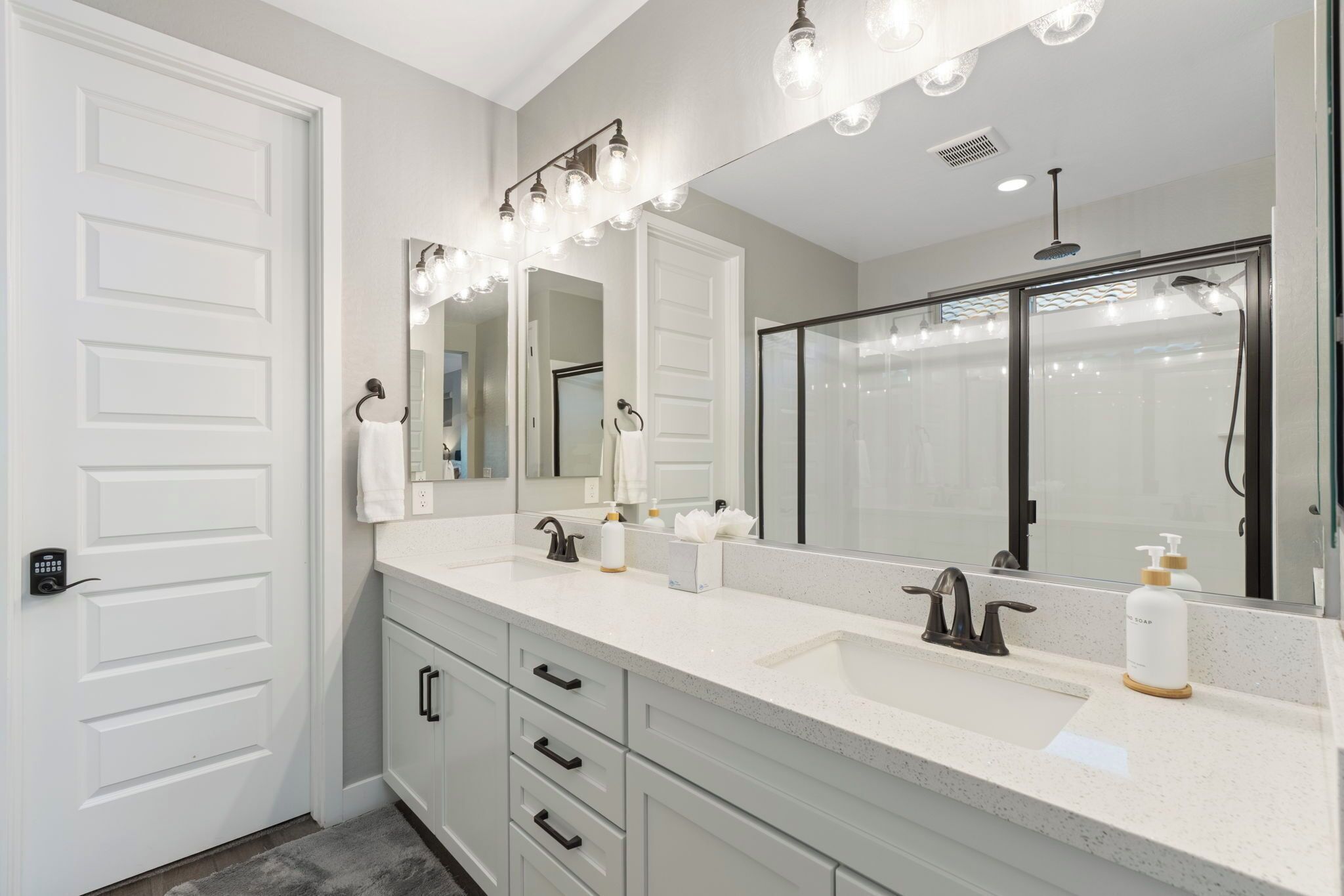 Een moderne badkamer met een dubbele wastafel, een grote spiegel en een douchecabine van glas.