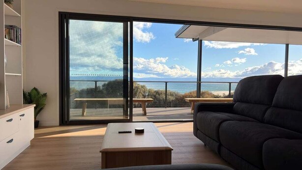 A modern living room with a large sliding glass door leading to a balcony overlooking a body of water and a bridge.