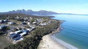 An aerial view of a coastal area with buildings, a beach, and mountains in the background.
