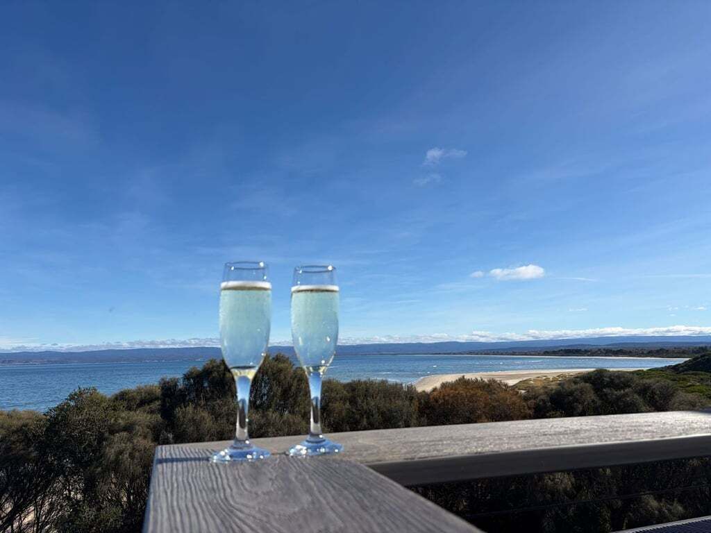 Zwei Gläser Weißwein auf einem Holztisch mit Blick auf das Meer und die Berge.