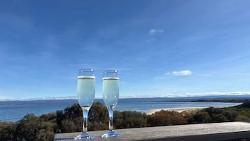 Zwei Gläser Weißwein auf einem Holztisch mit Blick auf das Meer und die Berge.