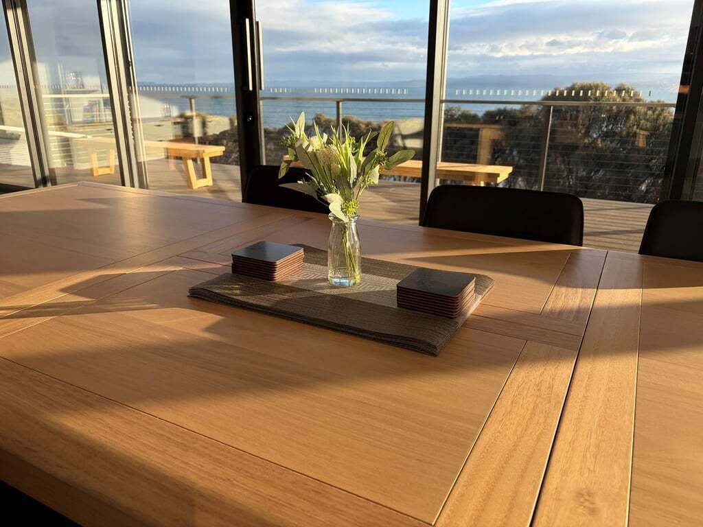 A conference table with a vase of flowers, a stack of books, and a view of the sea through large windows.