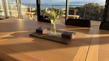 A conference table with a vase of flowers, a stack of books, and a view of the sea through large windows.