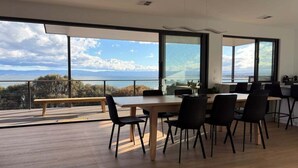 A modern dining area with a panoramic view of the sea and mountains.