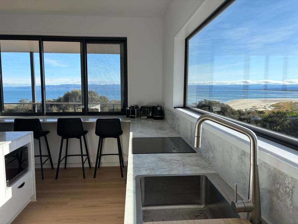 A modern kitchen with a large window, a sink, and bar stools.
