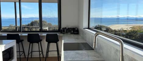 A modern kitchen with a large window, a sink, and bar stools.