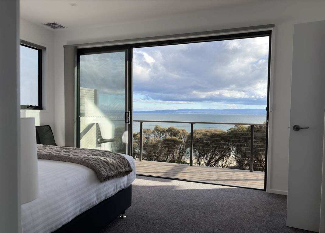 A bedroom with a large sliding glass door leading to a balcony with a view of the sea.