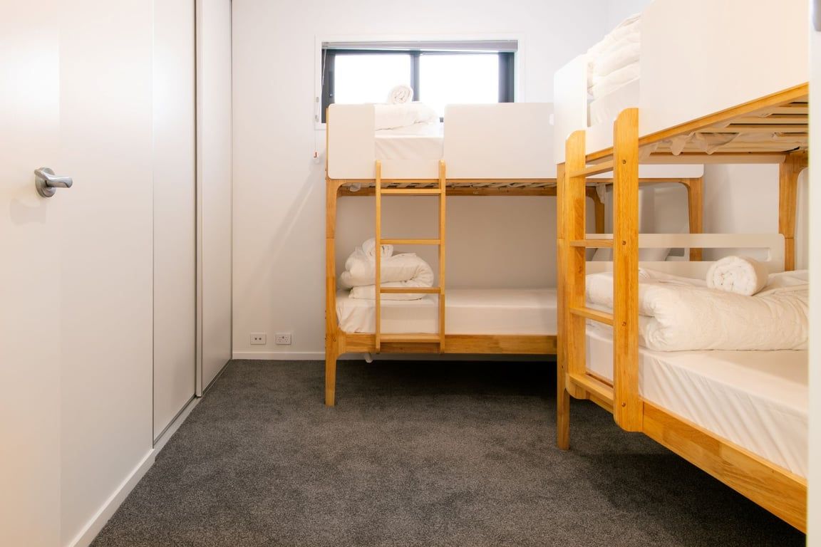 A bunk bed room with a window, carpeted floor, and a door.