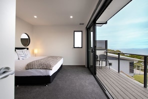 A bedroom with a bed, a bedside table, a mirror, and a window. - Beach Break - Freycinet Holiday Houses (Coles Bay)