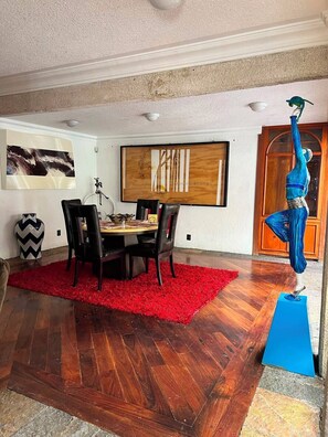 Uma área de jantar com uma mesa de madeira, cadeiras pretas, um tapete vermelho e uma escultura azul.