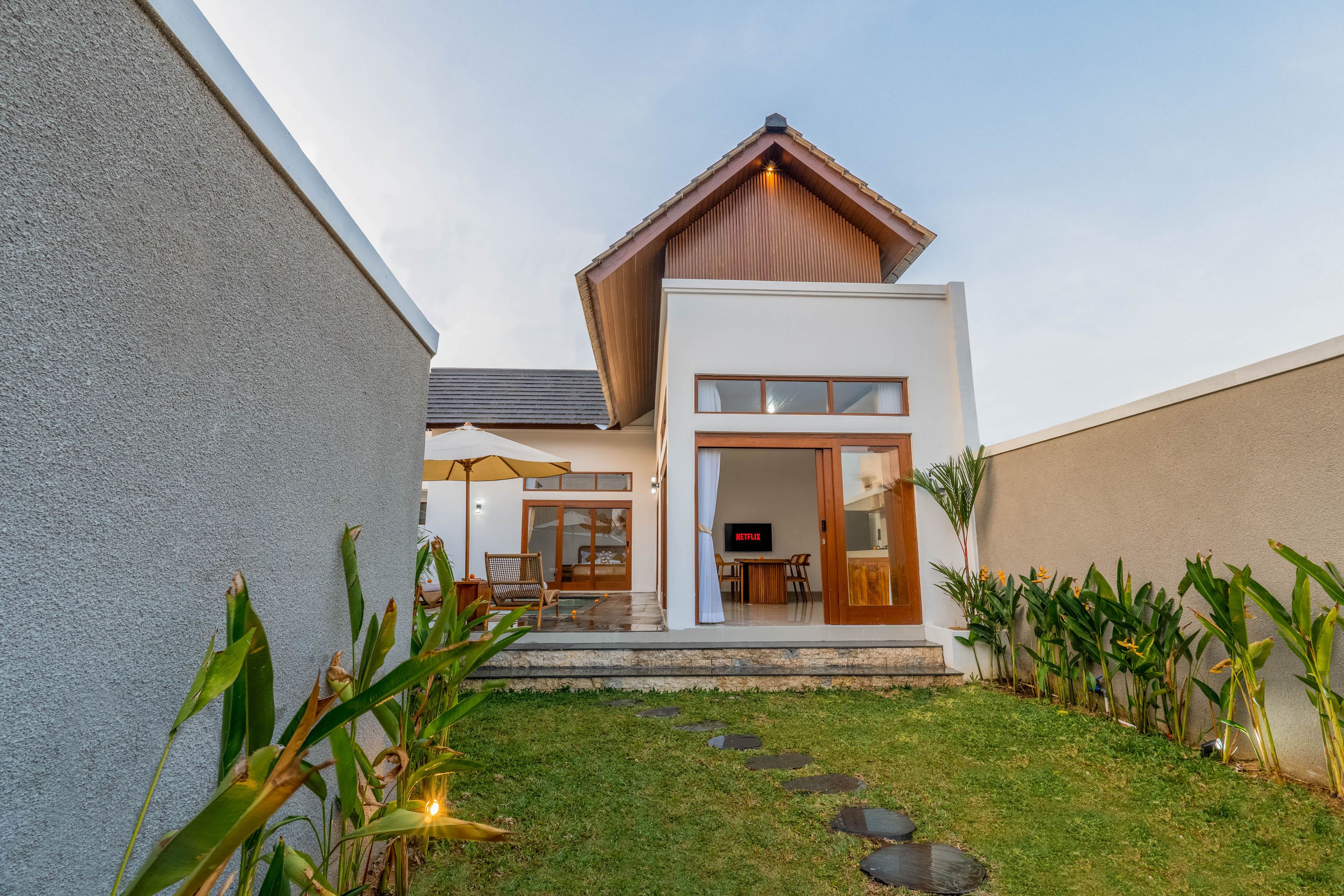 A modern house with a two-story structure, a visible living area with a sofa and a table, and a small garden with stepping stones.