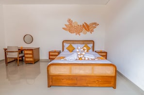 A bedroom with a wooden bed, a bedside table, a chair, and a wall decoration. - Royal Villa Nusa Dua (Bali)