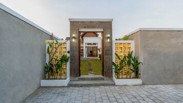 A modern entrance with a concrete pathway leading to a door, flanked by two lighted wall sconces and potted plants.