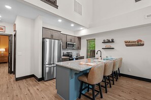 A modern kitchen with stainless steel appliances, a central island with bar stools, and a welcome sign on the wall. - More than a getaway, your best Branson family vacation memories start right here! (Hollister)