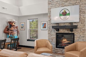 A living room with a stone fireplace, a bear statue, and a framed logo on the wall. - More than a getaway, your best Branson family vacation memories start right here! (Hollister)