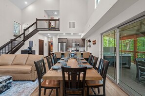 Un comedor amplio con una larga mesa de madera y varias sillas, una escalera que conduce a un nivel superior, y un gran ventanal corredero que ofrece vistas al exterior.