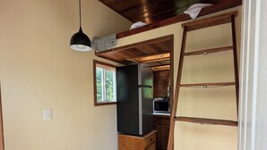 A compact kitchen with a refrigerator, a wooden ladder, and a hanging light fixture.