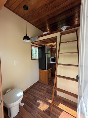 A compact kitchen with a refrigerator, a wooden ladder, and a hanging light fixture.