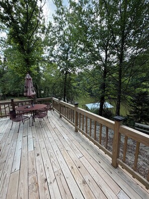 Une terrasse en bois avec une table et des chaises, entourée d’arbres et offrant une vue sur une étendue d’eau.