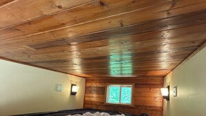 A bedroom with a wooden ceiling, a window, and a bed with a white blanket.