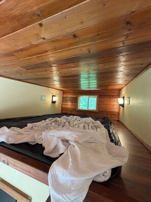 A bedroom with a wooden ceiling, a window, and a bed with a white blanket.