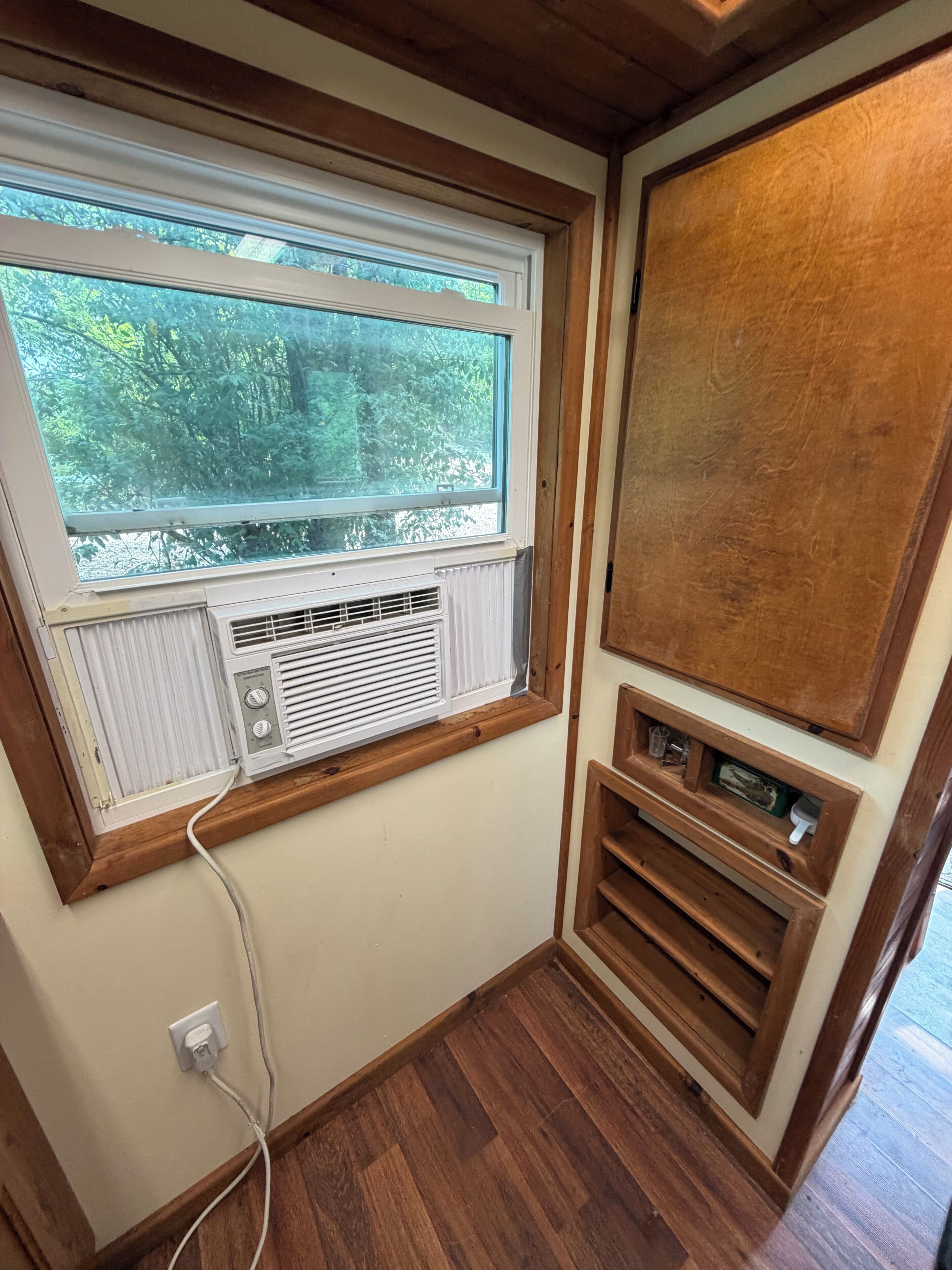 Une pièce dotée d’une fenêtre, d’un climatiseur, d’une armoire en bois et d’une prise de courant.