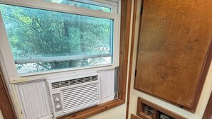 A room with a window, an air conditioning unit, a wooden cabinet, and a power outlet.