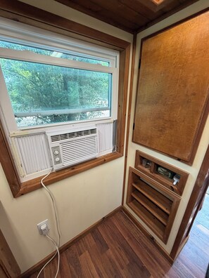 A room with a window, an air conditioning unit, a wooden cabinet, and a power outlet.