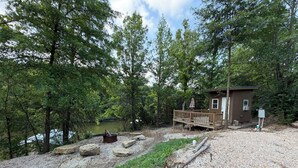 A cabin with a deck overlooking a lake, surrounded by trees.