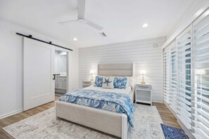 Un dormitorio con cama, mesitas de noche, ventilador de techo y ventana con persianas.